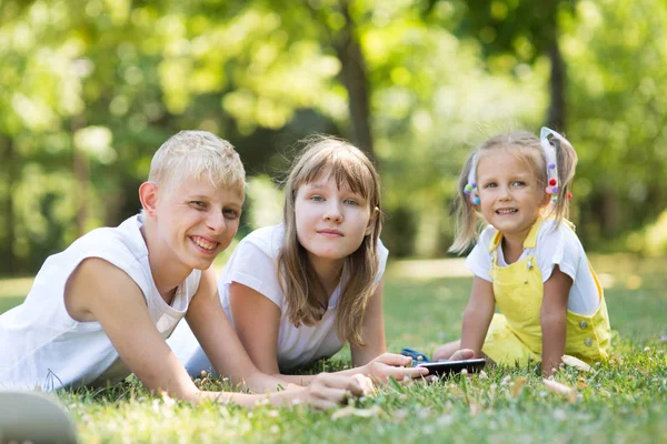 company of three children in the park are sitting on the grass with a phone