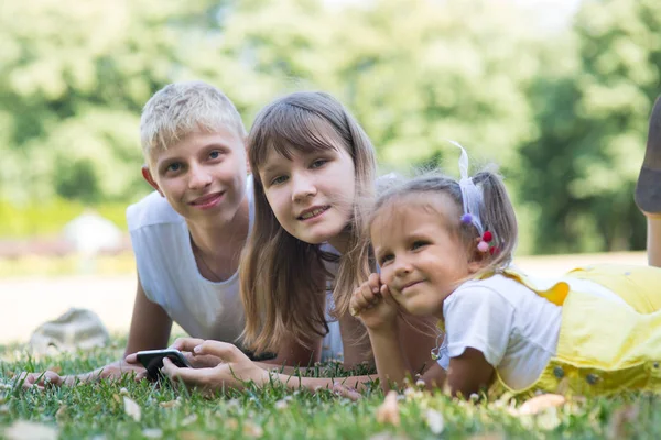 company of three children in the park are sitting on the grass with a phone