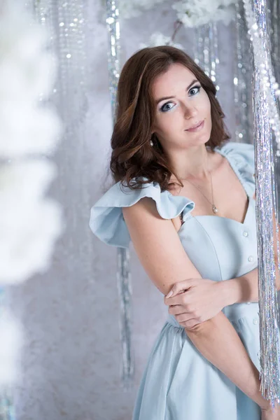 Beautiful young woman in silver studio in a blue dress