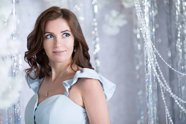 Beautiful young woman in silver studio in a blue dress