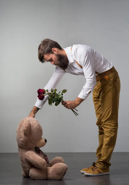 A man with roses and a big toy bear on a gray background