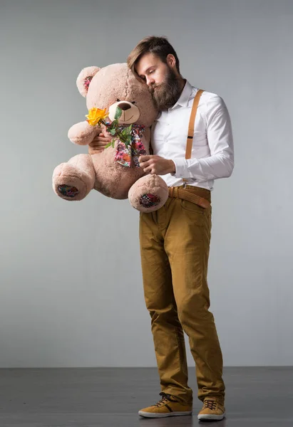 A man with roses and a big toy bear on a gray background