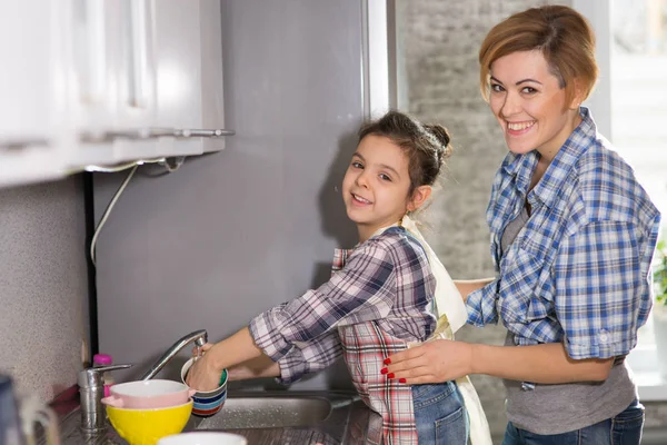 Mom and daughter do the dishes, woman and girl do the cleaning in the kitchen