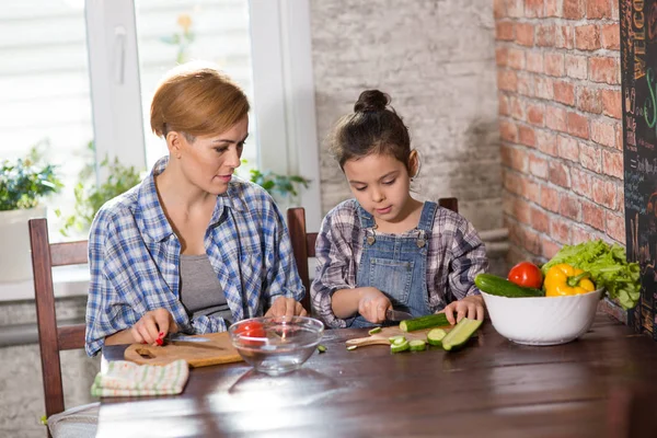Mom and daughter cook together at home, woman and girl prepare salad in the kitchen