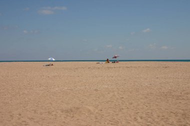 Denizin kenarında geniş yalnız plaj. Sadece üç turist uzakta onların şemsiye altında tutun. Denizde bir tekne olduğunu.