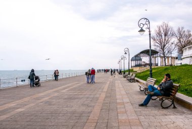 Köstence, Romanya. 19 Nisan 2019. Soğuk, karanlık Bir Nisan günü. Turistler sahil bulvarı boyunca yürürler. Köstence Karadeniz üzerinde önemli bir liman kenti yanı sıra popüler bir turizm.