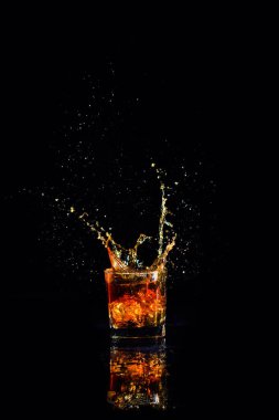 Siyah arka planda su sıçramış viski, bardakta brendi.