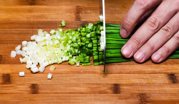 Готовить. Шеф-повар режет зеленый лук на кухне — стоковое фото