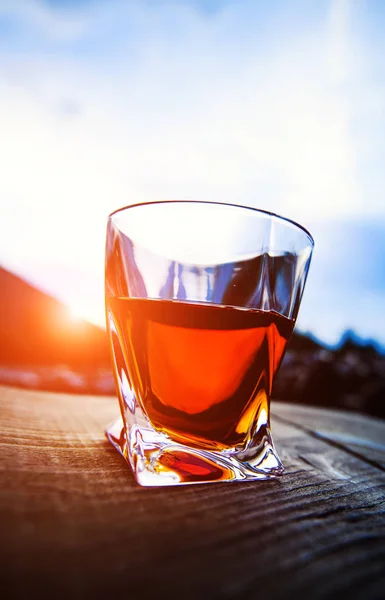 Shot of whiskey at sunset dramatic sky on mountain landscape bac — Stock Photo, Image