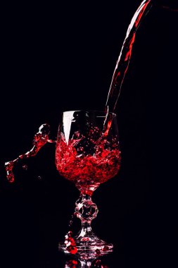 Red wine pouring into wine glass with splash, isolated on black