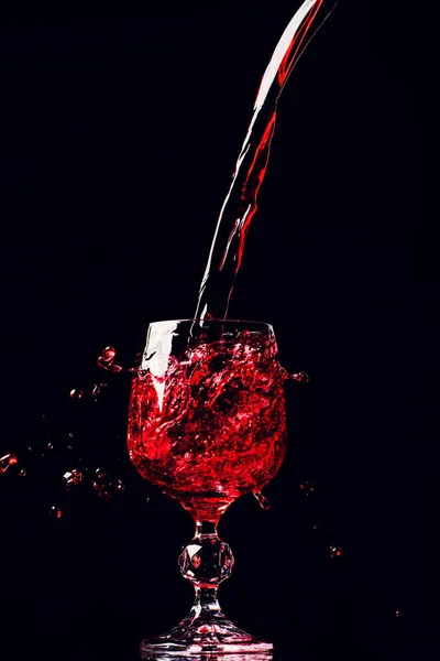 Κόκκινο κρασί ρίχνει σε ποτήρι κρασιού με βουτιά, απομονώνονται σε μαύρο — Φωτογραφία Αρχείου