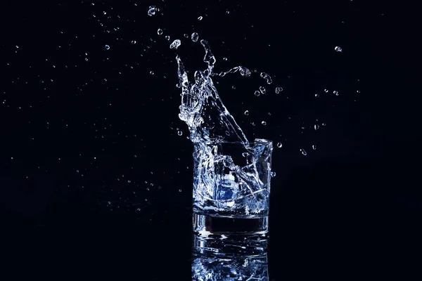 Acqua fredda isolata in un bicchiere con spruzzi e cubetti di ghiaccio su b — Foto Stock