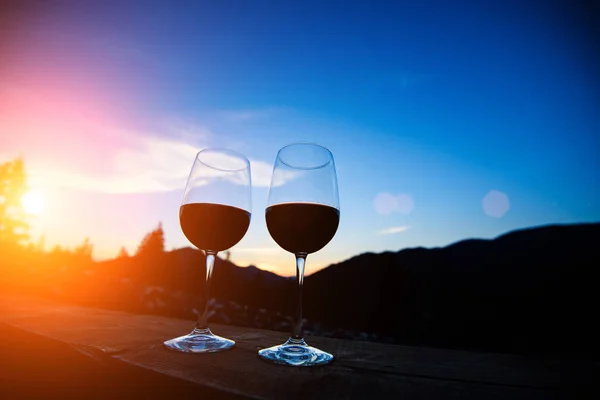 Two glasses of wine at sunset dramatic sky on mountain landscape