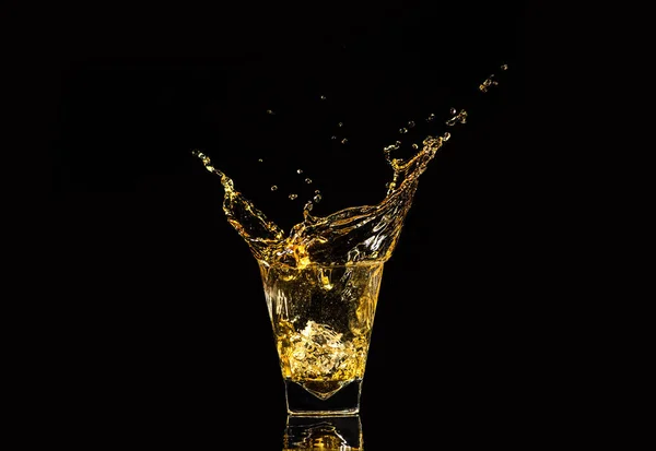 黒い背景の上に氷のキューブからのスプラッシュを持つウイスキーのガラス アルコールが飛び散った ウィスキーやコニャックやその他のアルコールの一種で — ストック写真