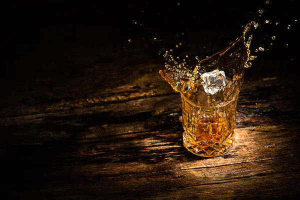 A glass of whiskey with splashes from the ice cube. glass with a splash of whisky on wooden background.