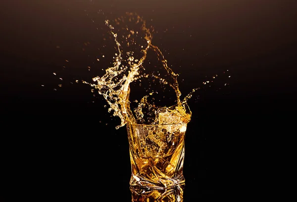黒い背景の上に氷のキューブからのスプラッシュを持つウイスキーのガラス アルコールのスプラッシュ — ストック写真