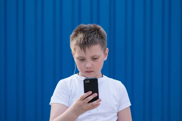 young boy stands with a phone in a white T-shirt