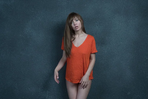 young beautiful girl posing in studio, standing in orange t-shirt