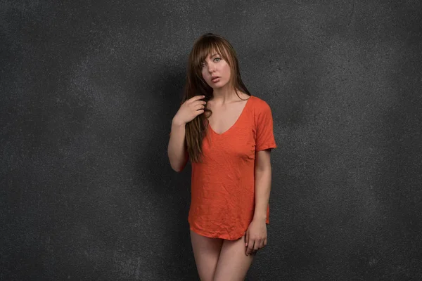 young beautiful girl posing in studio, standing in orange t-shirt