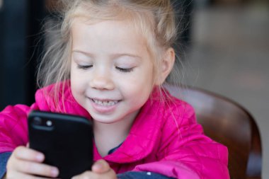 küçük kız bir telefonla bir kafede oturuyor