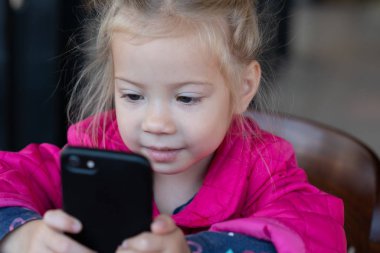 küçük kız bir telefonla bir kafede oturuyor