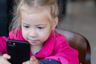 küçük kız bir telefonla bir kafede oturuyor