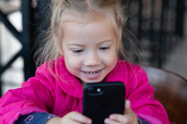 küçük kız bir telefon ile bir kafede oturuyor