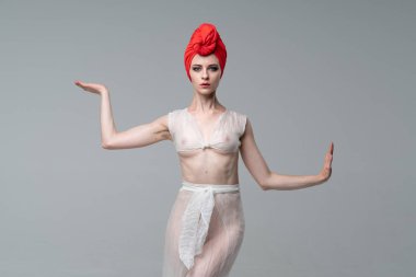 stüdyoda ayakta beyaz giysiler ve kırmızı bir şapka yoga yaparken genç güzel kız