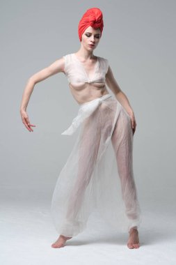 Stüdyoda çıplak poz veren genç ve güzel bir kız. Beyaz iç çamaşırı ve kırmızı şapkayla duruyor.