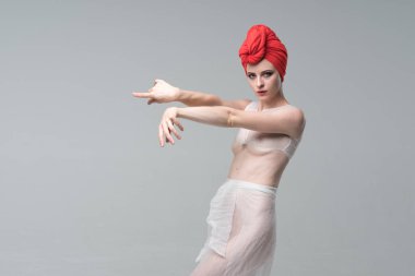 Stüdyoda çıplak poz veren genç ve güzel bir kız. Beyaz iç çamaşırı ve kırmızı şapkayla duruyor.