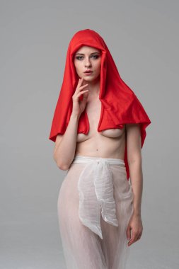 Stüdyoda poz veren genç ve güzel bir kız, beyaz şeffaf giysiler ve kırmızı bir eşarpla duruyor.