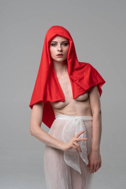 Stüdyoda poz veren genç ve güzel bir kız, beyaz şeffaf giysiler ve kırmızı bir eşarpla duruyor.