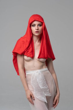 Stüdyoda poz veren genç ve güzel bir kız, beyaz şeffaf giysiler ve kırmızı bir eşarpla duruyor.
