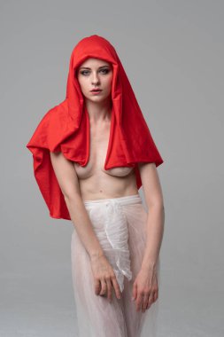 Stüdyoda poz veren genç ve güzel bir kız, beyaz şeffaf giysiler ve kırmızı bir eşarpla duruyor.