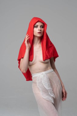 Stüdyoda poz veren genç ve güzel bir kız, beyaz şeffaf giysiler ve kırmızı bir eşarpla duruyor.