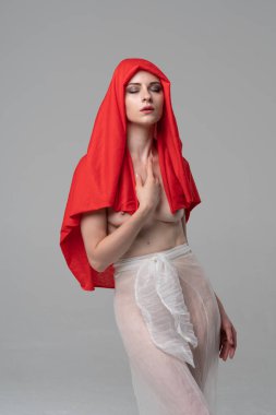 Stüdyoda poz veren genç ve güzel bir kız, beyaz şeffaf giysiler ve kırmızı bir eşarpla duruyor.