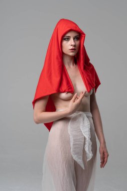 Stüdyoda poz veren genç ve güzel bir kız, beyaz şeffaf giysiler ve kırmızı bir eşarpla duruyor.