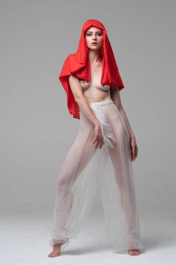 Stüdyoda poz veren genç ve güzel bir kız, beyaz şeffaf giysiler ve kırmızı bir eşarpla duruyor.