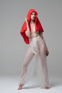 Stüdyoda poz veren genç ve güzel bir kız, beyaz şeffaf giysiler ve kırmızı bir eşarpla duruyor.