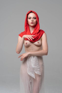 Stüdyoda poz veren genç ve güzel bir kız, beyaz şeffaf giysiler ve kırmızı bir eşarpla duruyor.