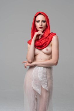 Stüdyoda poz veren genç ve güzel bir kız, beyaz şeffaf giysiler ve kırmızı bir eşarpla duruyor.