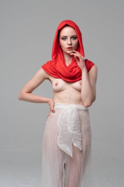 Stüdyoda poz veren genç ve güzel bir kız, beyaz şeffaf giysiler ve kırmızı bir eşarpla duruyor.