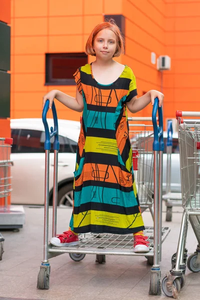 Mała Dziewczynka Pozowanie Zewnątrz Mieście Stojąc Kolorowej Sukni Wózku Supermarketu — Zdjęcie stockowe
