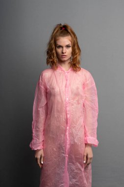 genç güzel kız stüdyoda poz, pembe bir yağmurluk ayakta