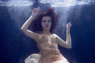 genç güzel kız çıplak sualtı poz, altın bir elbise içinde bir havuzda yüzme