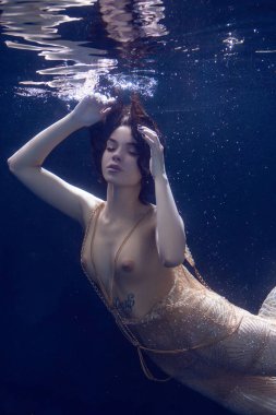 genç güzel kız çıplak sualtı poz, altın bir elbise içinde bir havuzda yüzme