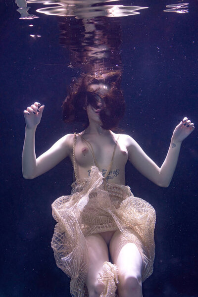 young beautiful girl posing nude underwater, swimming in a pool in a golden dress