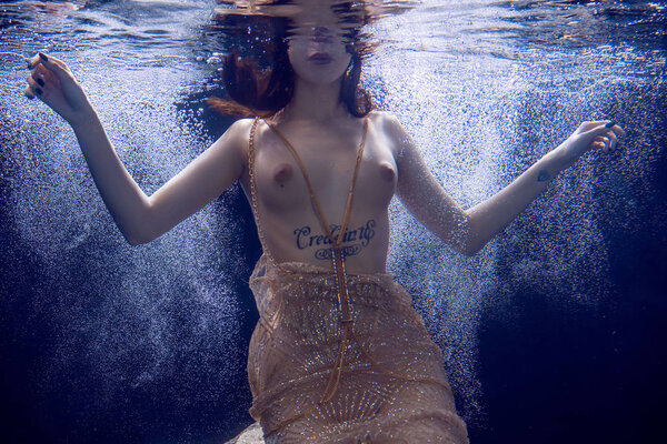 young beautiful girl posing nude underwater, swimming in a pool in a golden dress