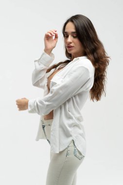 Stüdyoda beyaz gömlek ve beyaz kotla poz veren güzel bir kız.