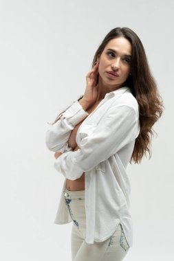 Stüdyoda beyaz gömlek ve beyaz kotla poz veren güzel bir kız.